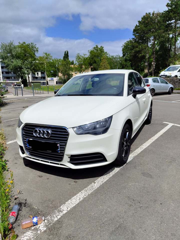 Audi A1 blanche vue de trois quarts avant sur un parking, sous un ciel dégagé