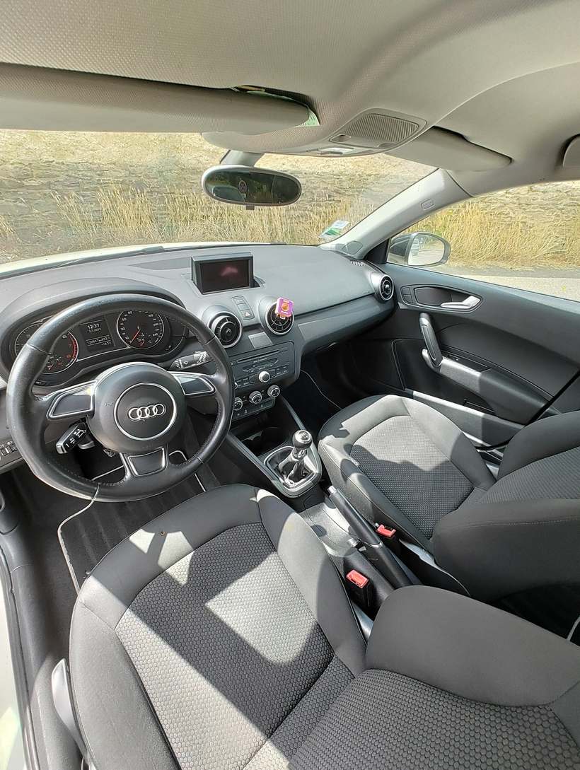Habitacle d’une Audi A1 : tableau de bord, volant, console et sièges avant en tissu gris propres