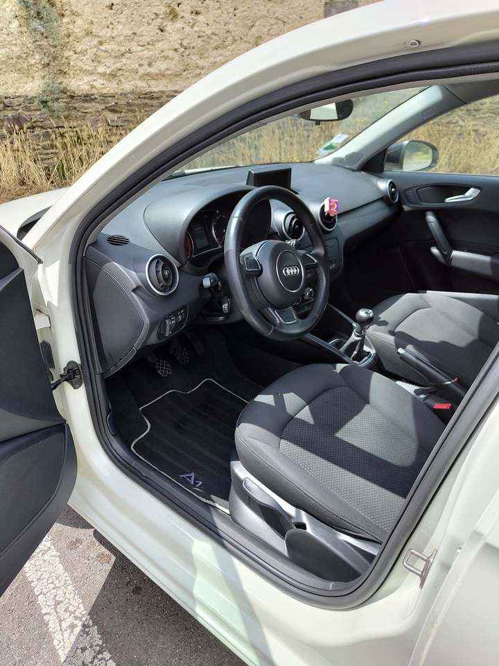 Poste de conduite d’une Audi A1 vu par la portière ouverte : siège, volant, tapis et contre-porte