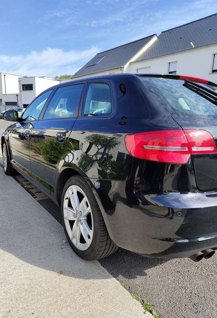 Audi A3 Sportback noire vue de trois quarts arrière, carrosserie brillante reflétant les arbres, jantes argentées propres