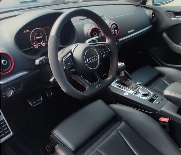 Habitacle d’une Audi RS3 : volant sport, console centrale et sièges en cuir noir à surpiqûres rouges