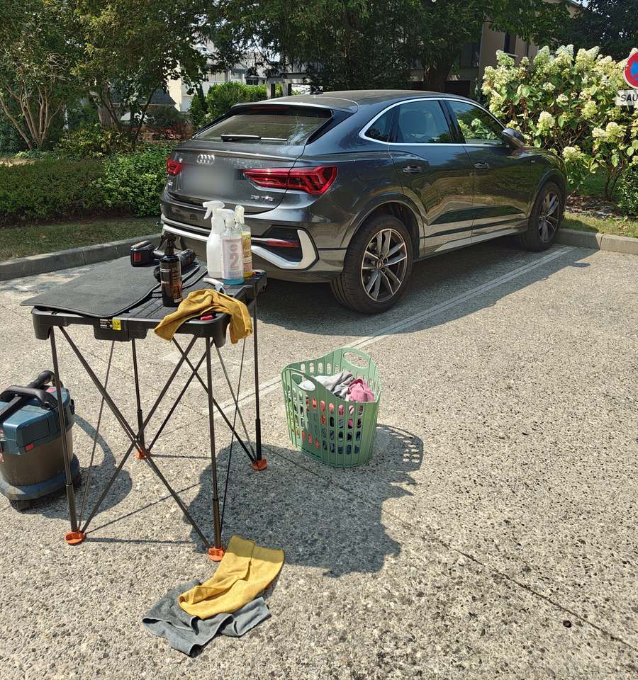 Matériel Starwash installé sur un parking derrière une Audi Q3 Sportback grise : table pliante avec tapis de sol et produits, aspirateur, panier de microfibres