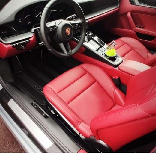 Siège conducteur en cuir rouge et tableau de bord d’une Porsche 911, portière ouverte